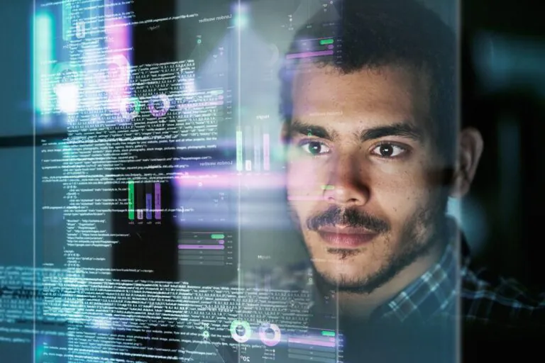 jovem pardo de bigode vê em vidro reflexo de um código em desenvolvimento para ilustrar artigo sobre a profissão de engenheiro de software