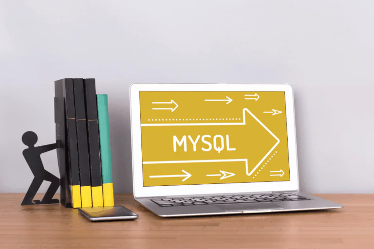 Foto representando artigo sobre o que é MySQL através de um notebook aberto; o fundo de tela é amarelo escuro e tem a inscrição MySQL em letras brancas, bem como setas brancas ilustradas indicando para a direita. Na mesa, ao lado esquerdo, um celular e quatro livros sendo sustentados por um divertido suporte para livros.