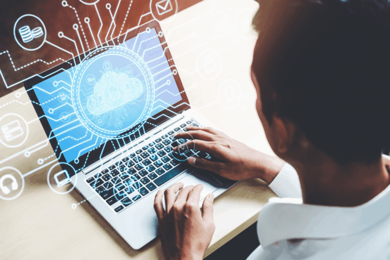 homem de camisa branca utiliza um laptop que exibe imagens holográficas de ícones e gráficos relacionados a consultoria em cloud computing, incluindo nuvens, cadeados de segurança, símbolos de redes e barras de dados. Ele está focado na tela, indicando um ambiente de trabalho tecnológico e digital.