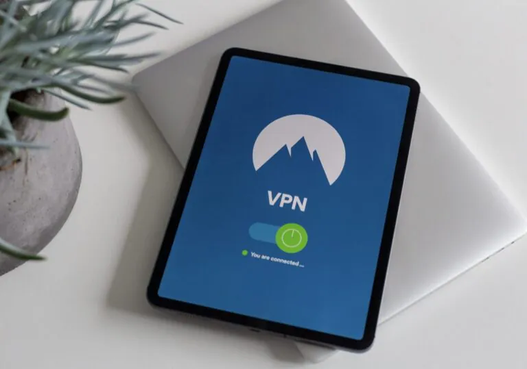 Exemplificando como a VPN mantém a privacidade dos dados, a imagem mostra um tablet preto sobre uma superfície branca e plana, com um tablet slim fechado embaixo, um vaso de planta em concreto ao lado e com a tela exibindo um fundo azul, uma logo redonda com uma montanha, a sigla VPN abaixo, um símbolo de conectado e abaixo, escrito "You are connected..." ao lado de um círculo verde.