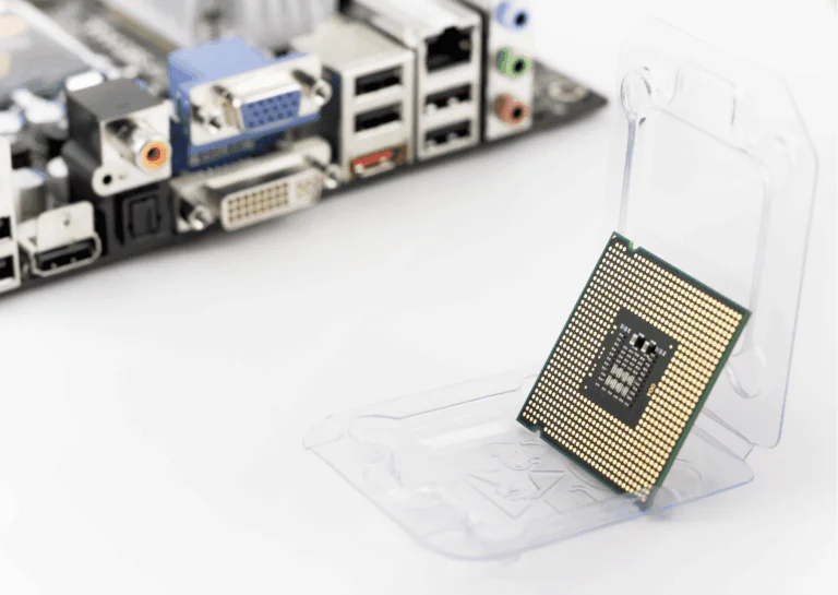 Exemplificando a evolução dos processadores, estão sobre uma superfície branca, ao fundo, portas e entradas de computadores e, em destaque, um chip de processador verde com placa dourada disposto sobre uma superfície de apoio transparente que o deixa em pé e levemente inclinado para trás.